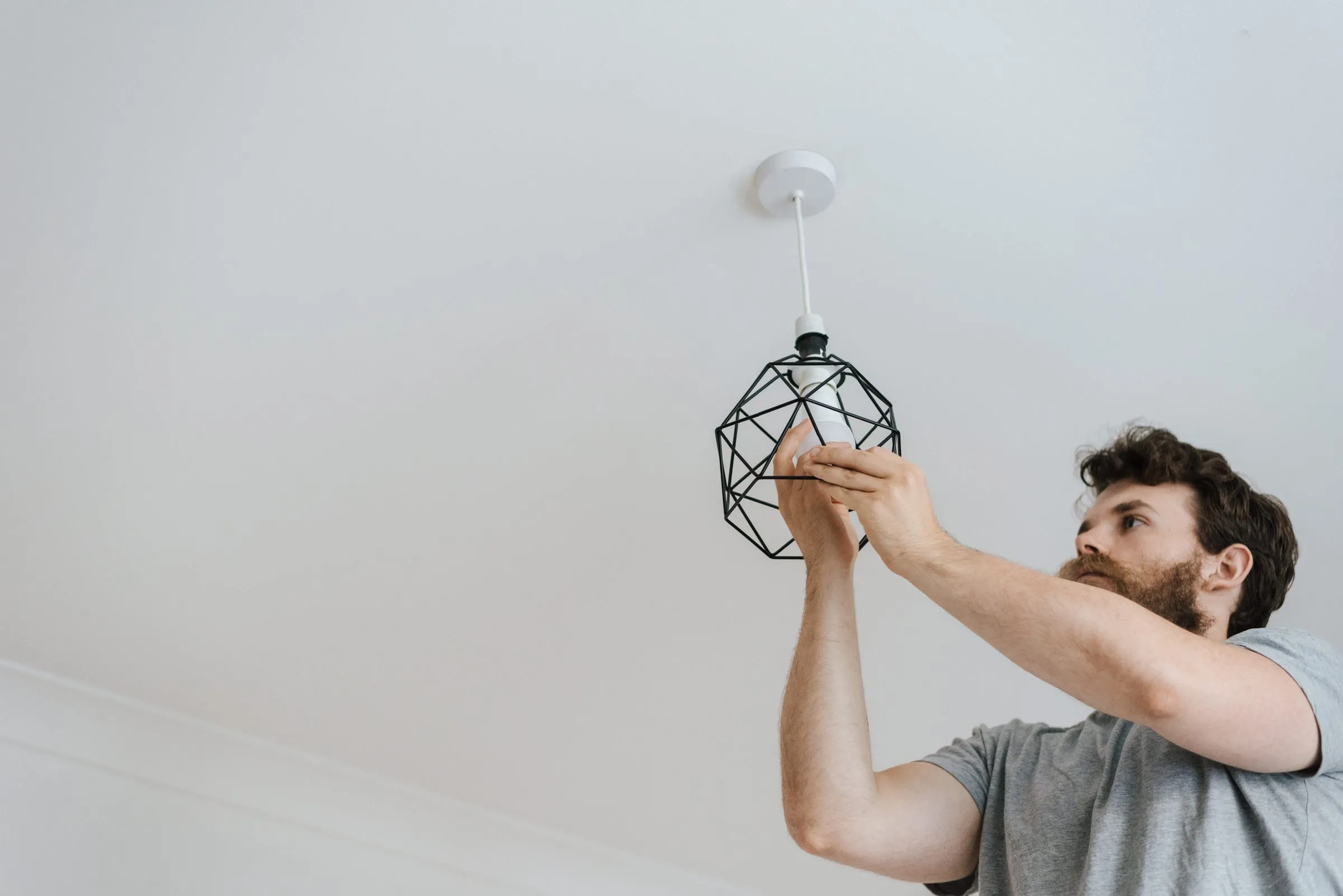 Électricien qui pose une suspension au plafond d’une pièce blanche